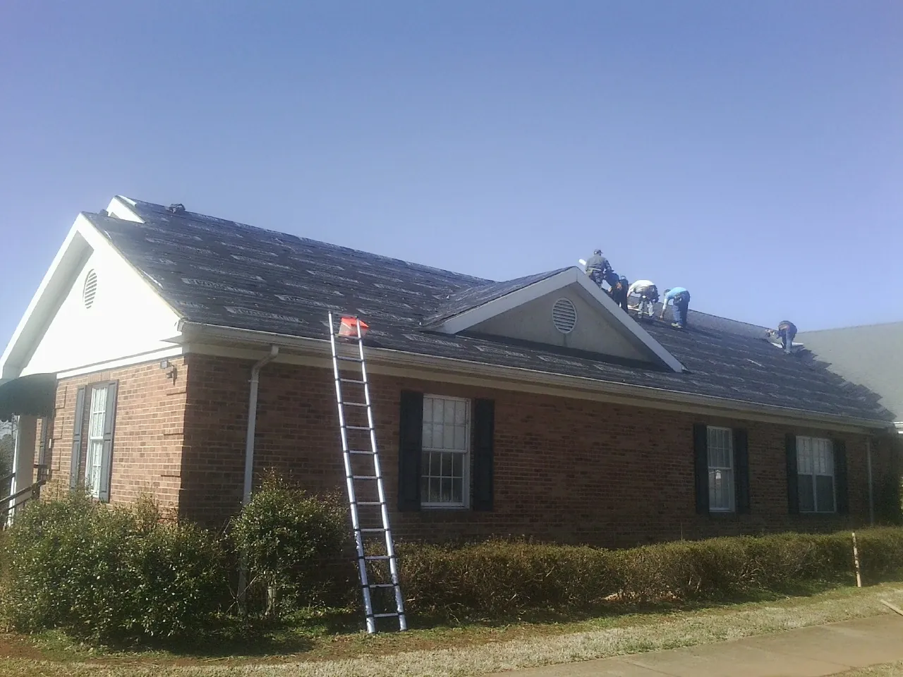 Crew tearing shingles off a brick ranch roof with a ladder set — Metal Roof Repair work by our crew in Otter Rock