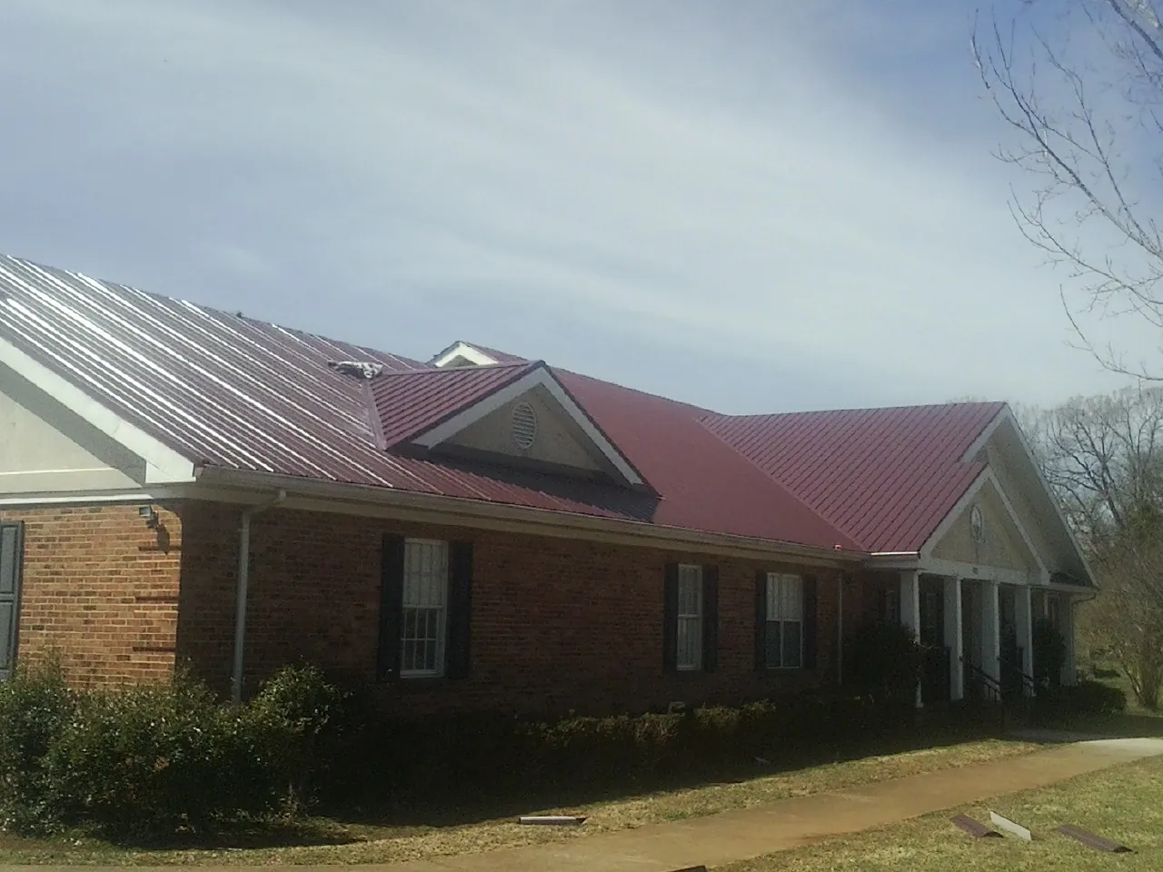 Red metal roof with gabled entries on a long brick building, from a Hail Damage Roof Repair job in Otter Rock