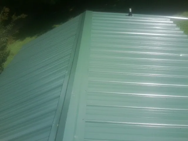 New green metal panels meeting at the ridge of a roof — Flat Roof Repair work by our crew in Otter Rock