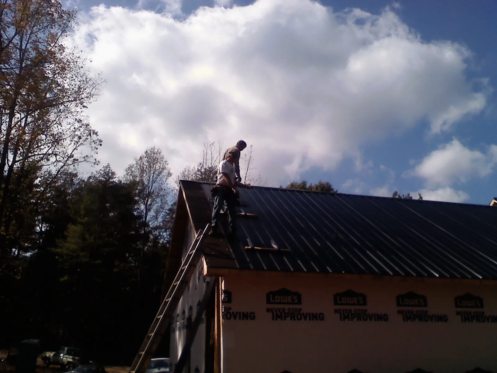 Roofer fastening dark metal panels high against a cloudy sky, from a Roof Inspection job in Otter Rock