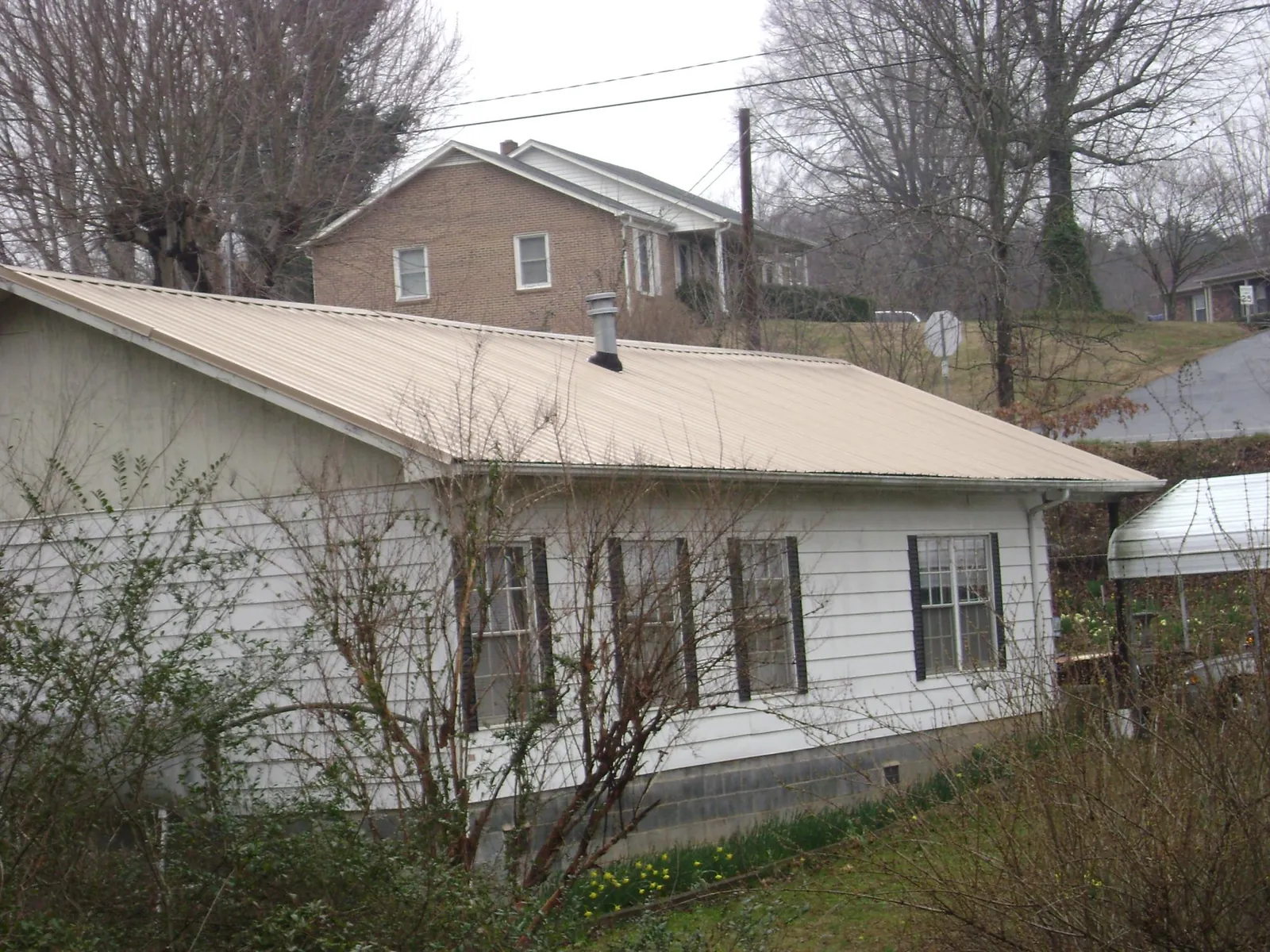 Tan metal roof on a white sided house set into a hillside — Commercial Roofing by Roofing Brothers in Otter Rock
